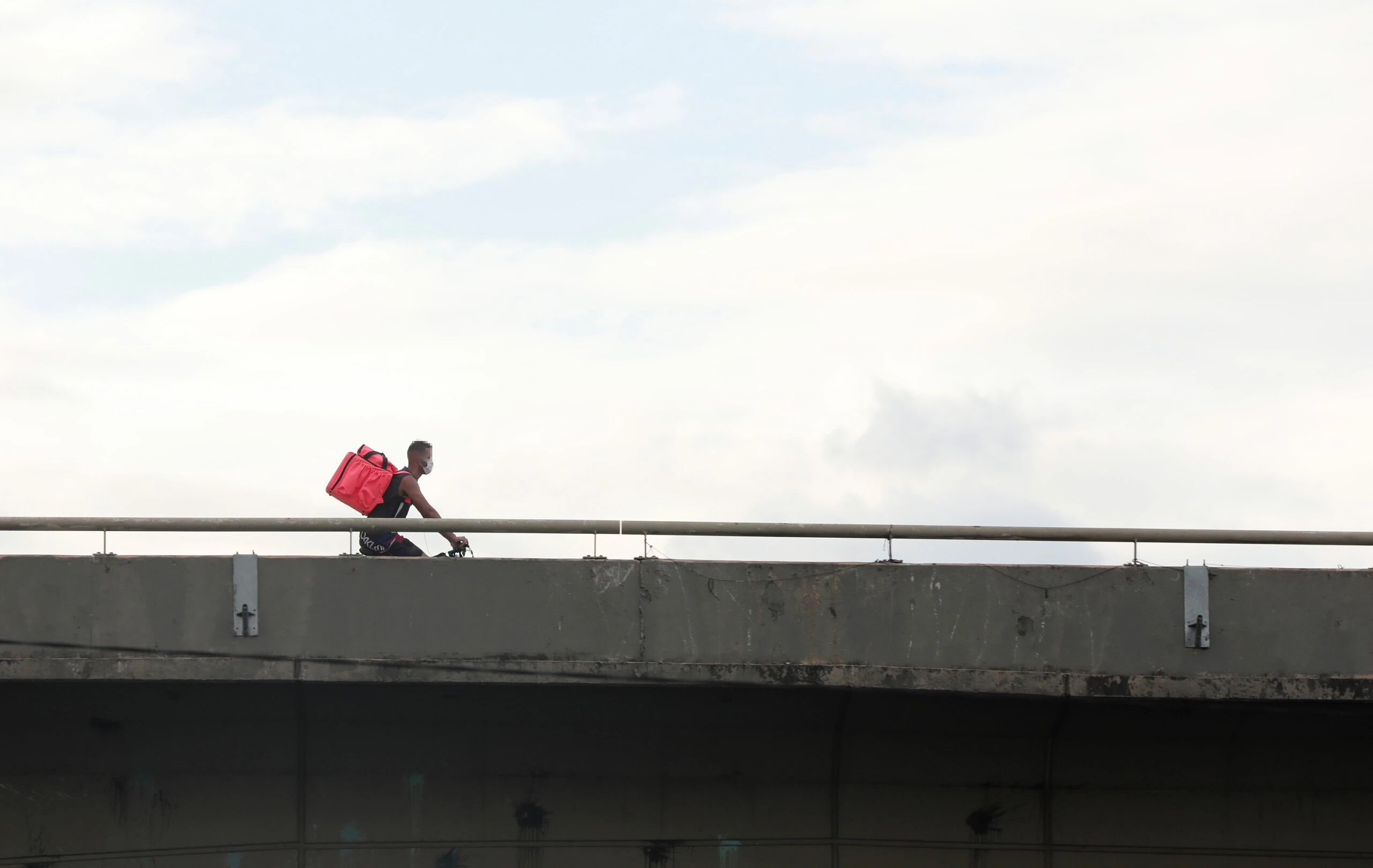 De bicicleta e máscara, entregador percorre viaduto de São Paulo a serviço de aplicativos de entregas.