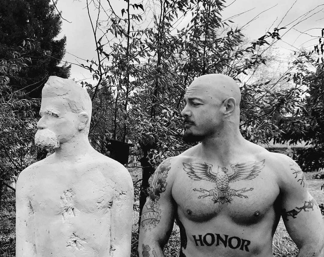 Jack Donovan posa ao lado de uma estátua de Nietzsche.