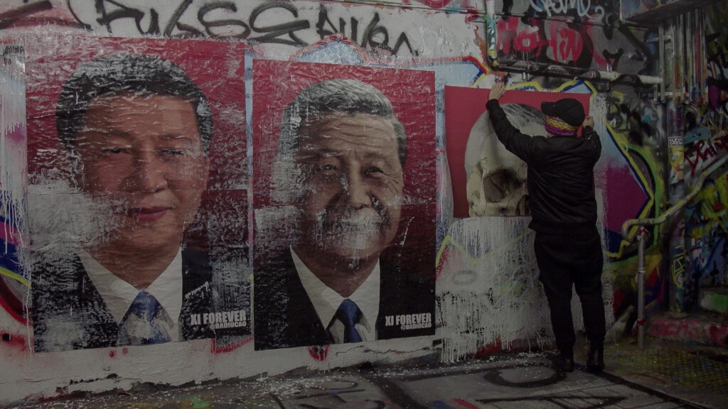 Em um frame de “China’s Artful Dissident” (Habilidoso dissidente da China), Badiucao aparece em Melbourne, na Austrália, com uma peça que ele criou em resposta a uma alteração feita em 2018 na constituição chinesa, permitindo que o presidente Xi Jinping permanecesse no poder pelo resto da vida.