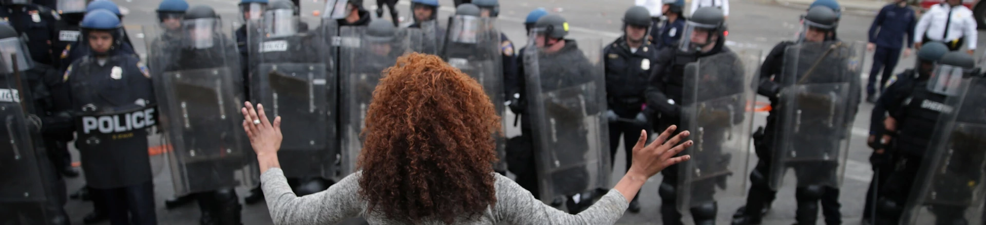 BALTIMORE, MD - APRIL 27: A woman faces down a line of Baltimore Police officers in riot gear during violent protests following the funeral of Freddie Gray April 27, 2015 in Baltimore, Maryland. Gray, 25, who was arrested for possessing a switch blade knife April 12 outside the Gilmor Homes housing project on Baltimore's west side. According to his attorney, Gray died a week later in the hospital from a severe spinal cord injury he received while in police custody. (Photo by Chip Somodevilla/Getty Images) BALTIMORE, MD - APRIL 27: A woman faces down a line of Baltimore Police officers in riot gear during violent protests following the funeral of Freddie Gray April 27, 2015 in Baltimore, Maryland. Gray, 25, who was arrested for possessing a switch blade knife April 12 outside the Gilmor Homes housing project on Baltimore's west side. According to his attorney, Gray died a week later in the hospital from a severe spinal cord injury he received while in police custody. (Photo by Chip Somodevilla/Getty Images)